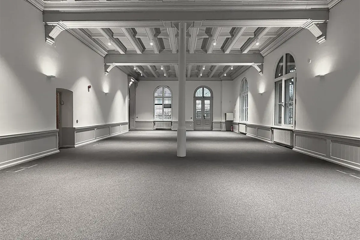 Virtual staging of an open plan office with white desks and plants in a historic hall with arched windows, made from a photo of the empty room with RenderAI